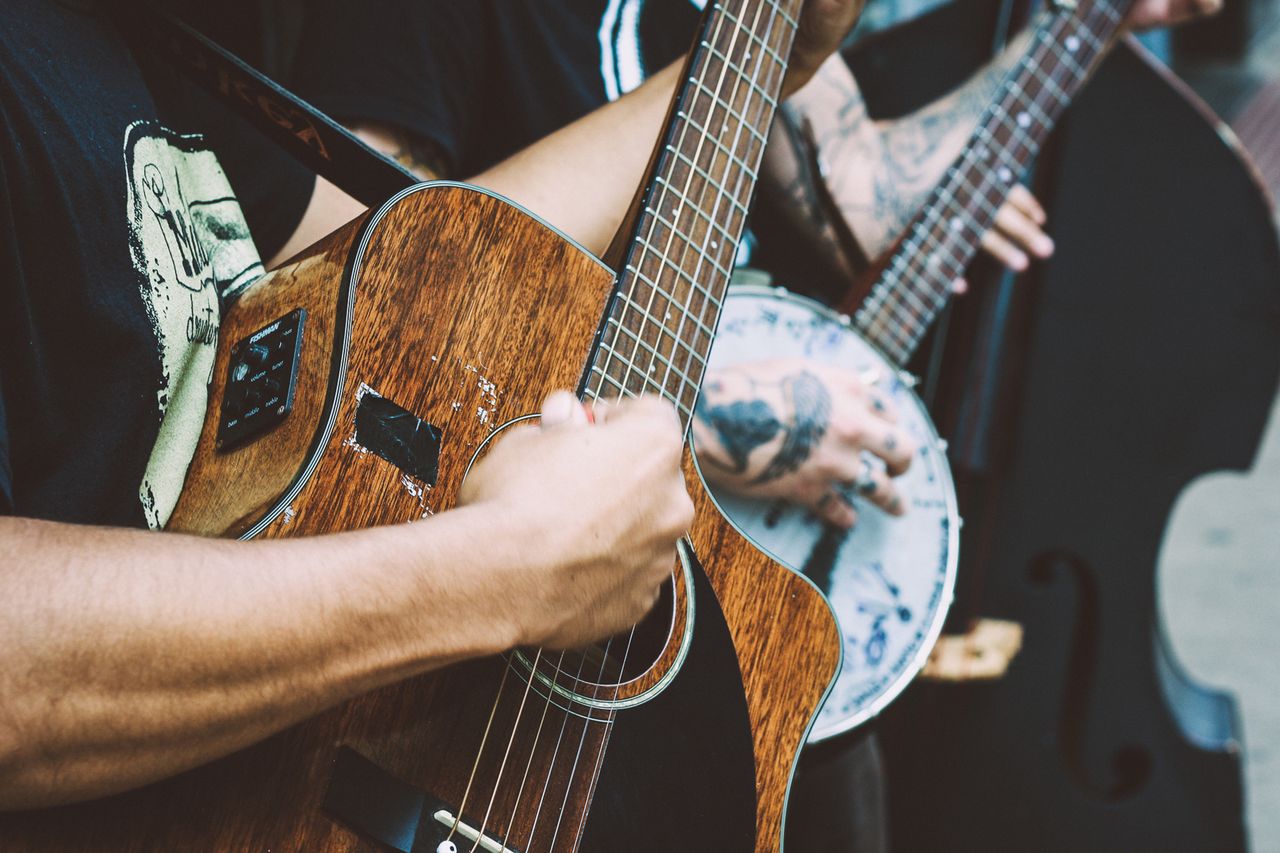 Close-up of musicians strumming acoustic and banjo guitars in a vibrant street performance.