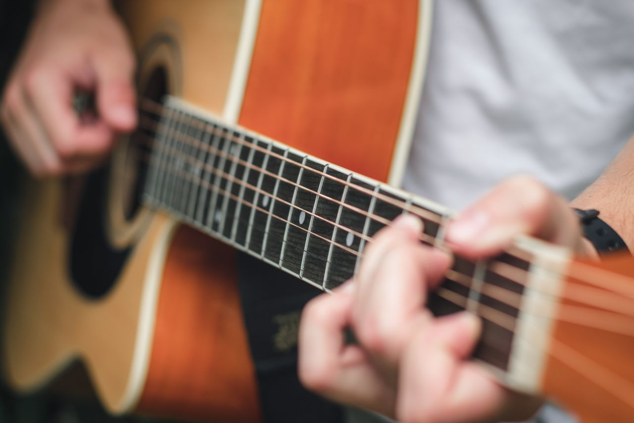 Crop anonymous male musician playing guitar while performing song and spending time doing hobby